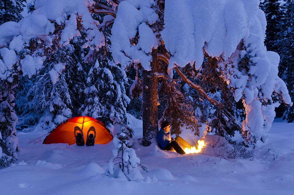 Mann ute i snøen med telt og bål