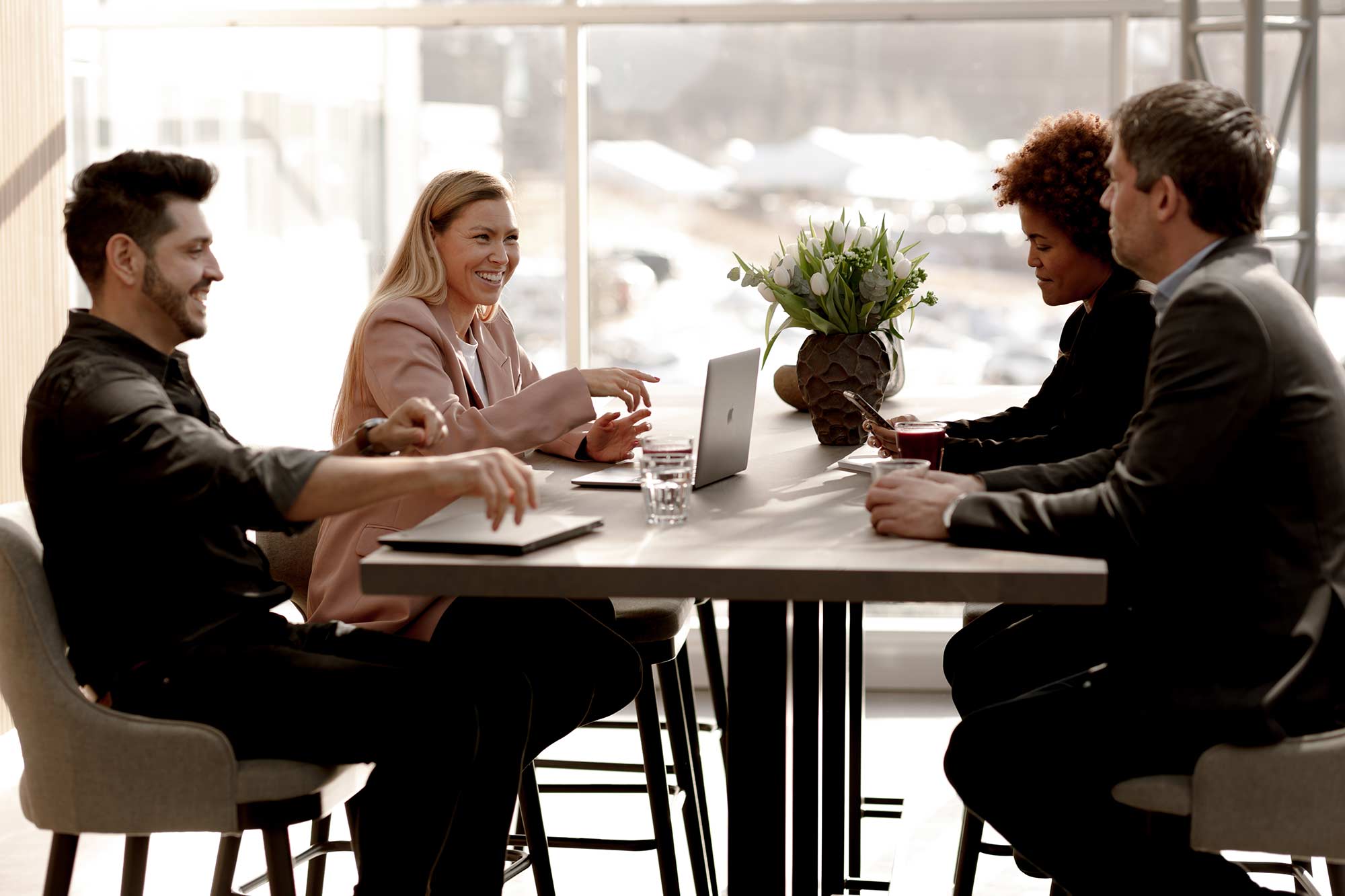 Fire personer sitter ved et bord og prater i kontorfellesskap/coworking