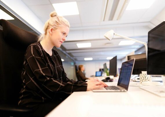 En dame sitter og jobber på en mac i et kontorlandskap