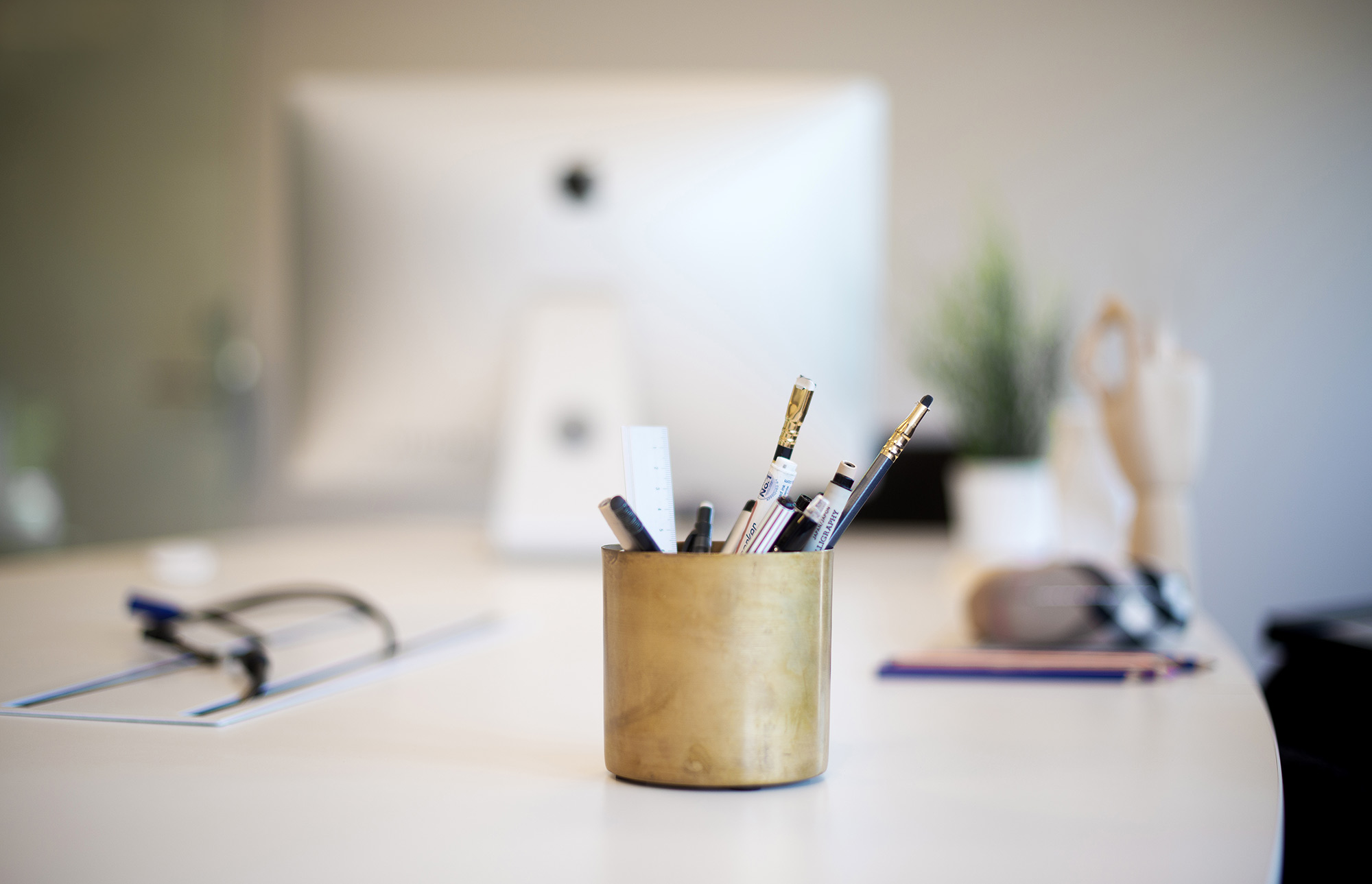 Skrivebord med mac, kopp med penner og blyanter og andre kontorartikler
