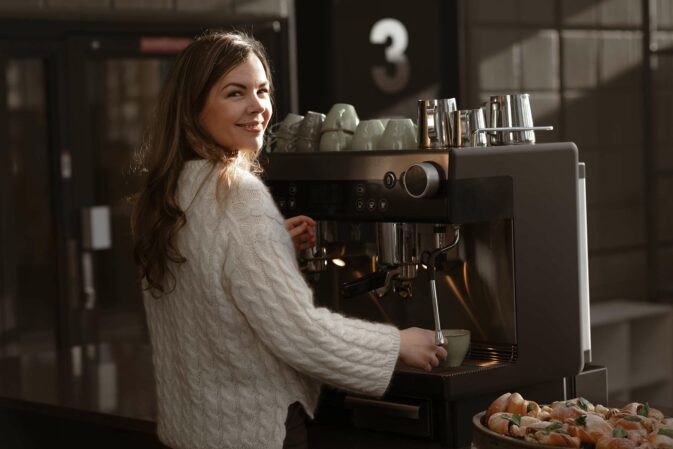 Dame står ved kaffemaskin og lager kaffe i Skullerud Park
