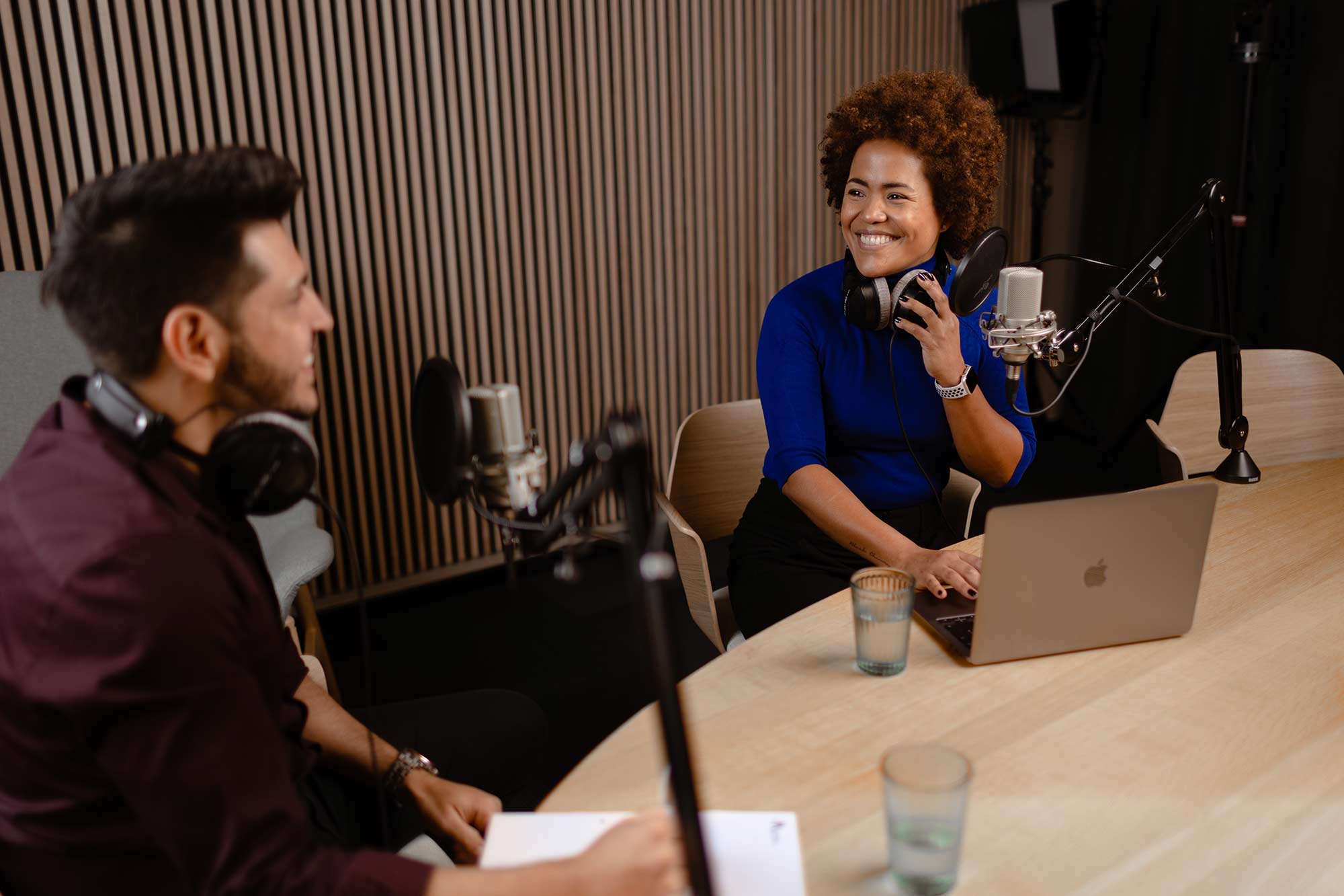 Dame og mann smiler og prater inn i podcast-mikrofoner